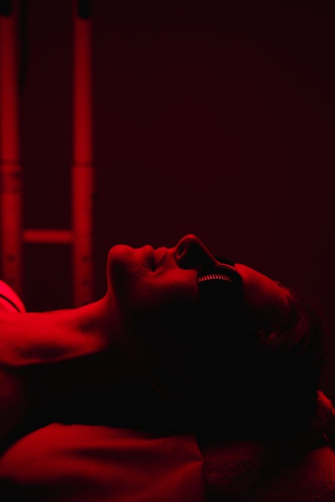 A woman laying under red light therapy panel with a pair of black goggles.